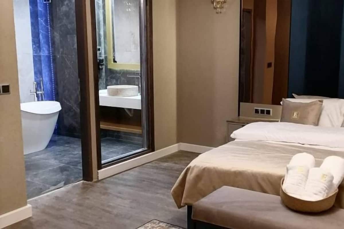 A hotel room with a large bed, a bathroom with a bathtub, and a sliding glass door leading to a shower area.