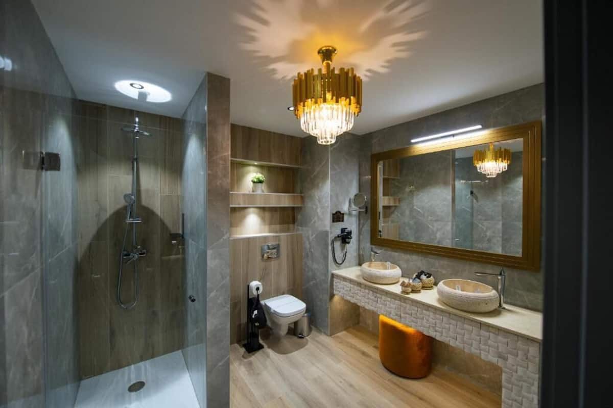 A modern bathroom with a walk-in shower, a toilet, a sink with a large mirror, and a chandelier.