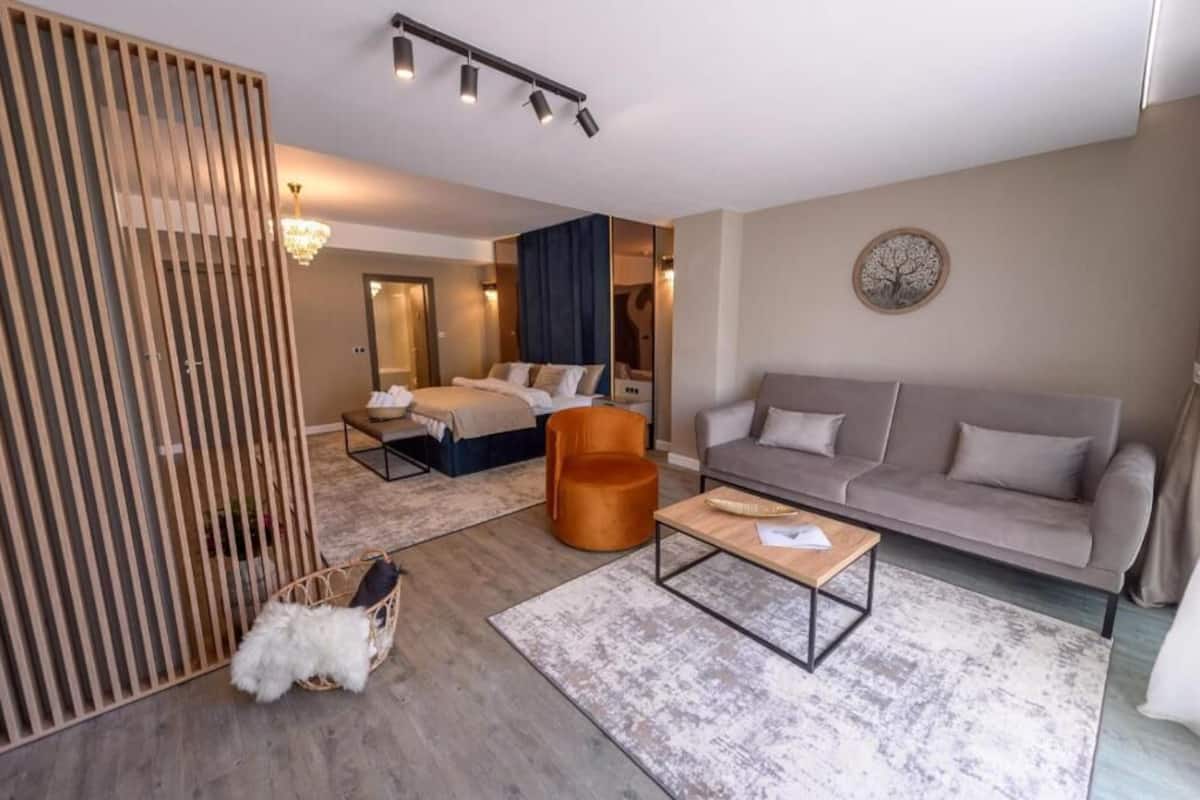 A modern hotel room with a bed, a sofa, a coffee table, and a decorative mirror.