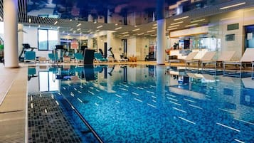 Una piscina interior con agua cristalina, rodeada de sillas de descanso y equipo de ejercicio.