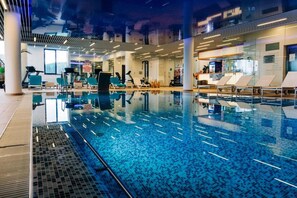 An indoor swimming pool with clear water, surrounded by lounge chairs and exercise equipment. - Elexus Poiana Brasov (Brasov)