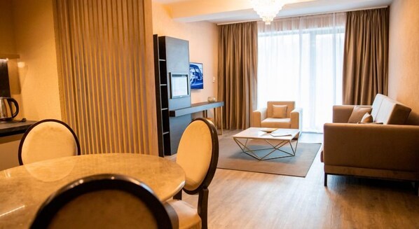 A hotel room with a dining table, chairs, a sofa, a TV, and curtains. - Elexus Poiana Brasov (Brasov)