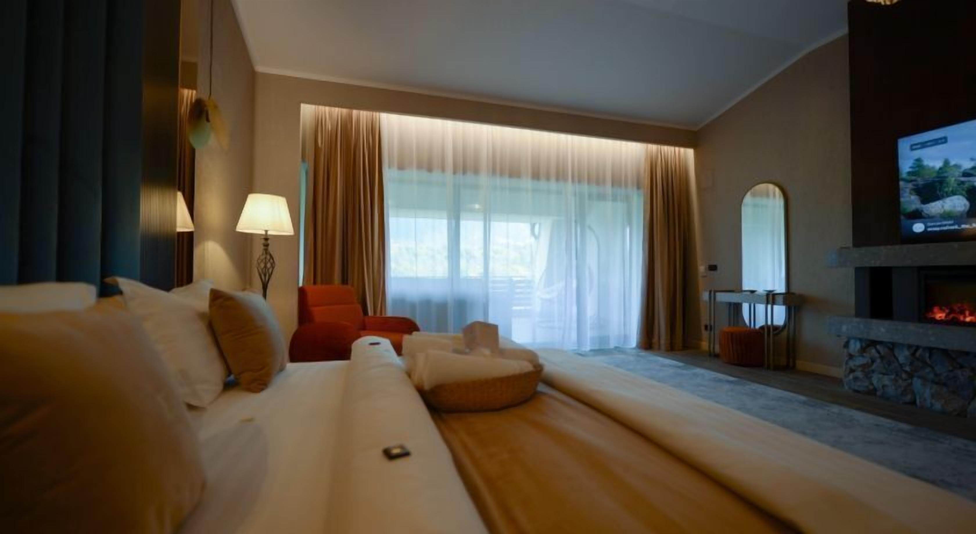 Une chambre d’hôtel avec un grand lit, un fauteuil rouge, un canapé, une télévision et une cheminée.