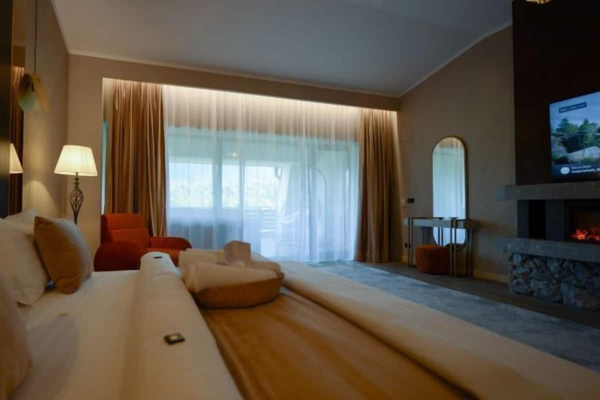 A hotel room with a large bed, a red armchair, a sofa, a TV, and a fireplace.