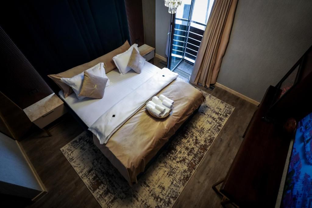 A hotel room with a bed, pillows, a bedside table, a rug, and a view of the outside.