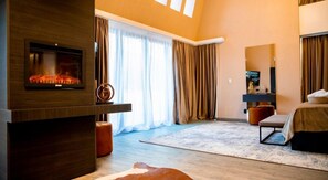 A modern hotel room with a fireplace, a large bed, a seating area, and a television. - Elexus Poiana Brasov (Brasov)