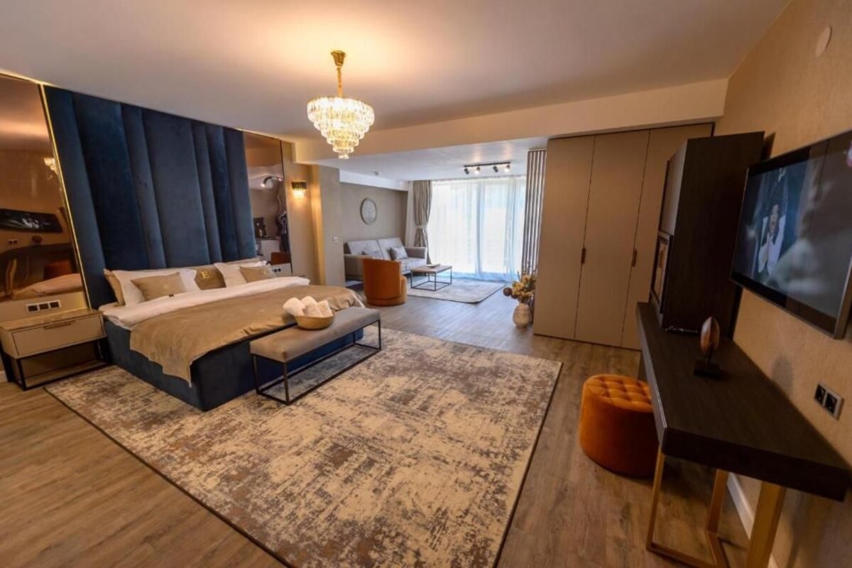 A modern bedroom with a large bed, a TV, and a chandelier.