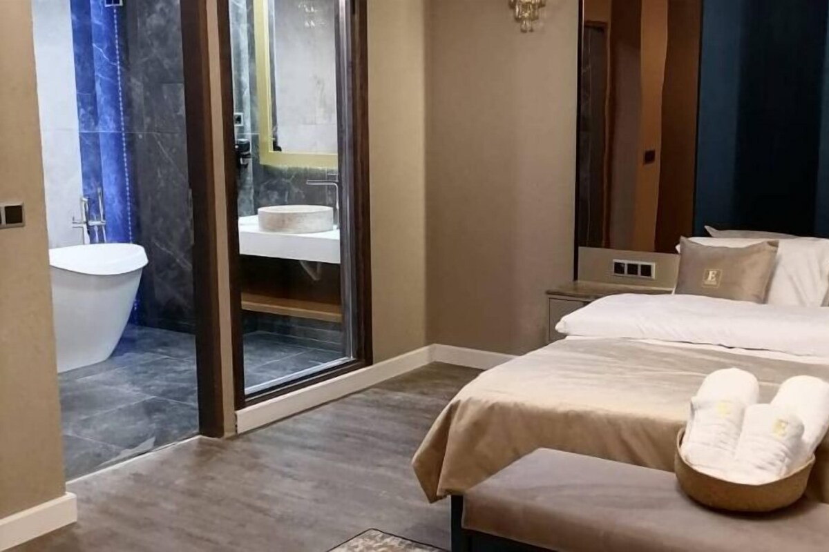 A hotel room with a large bed, a bathroom with a bathtub, and a sliding glass door leading to a shower area.