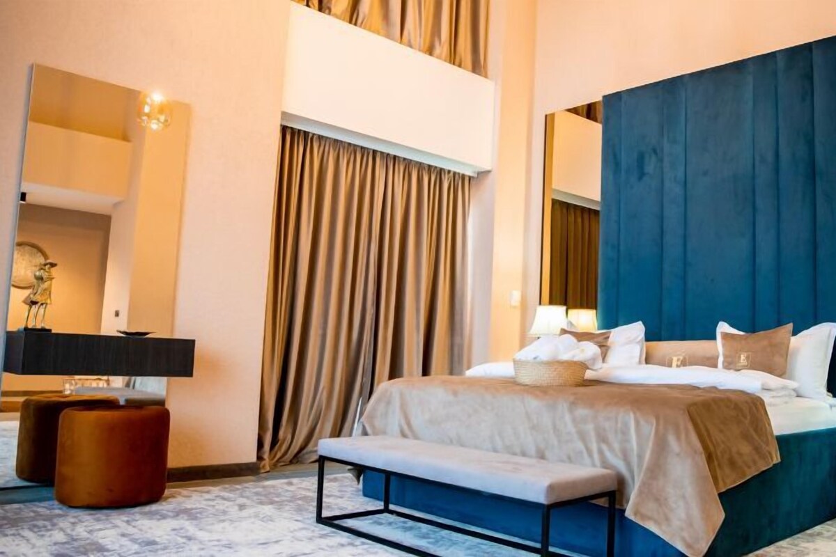 A modern hotel room with a large bed, a bench, a desk, and a chair.