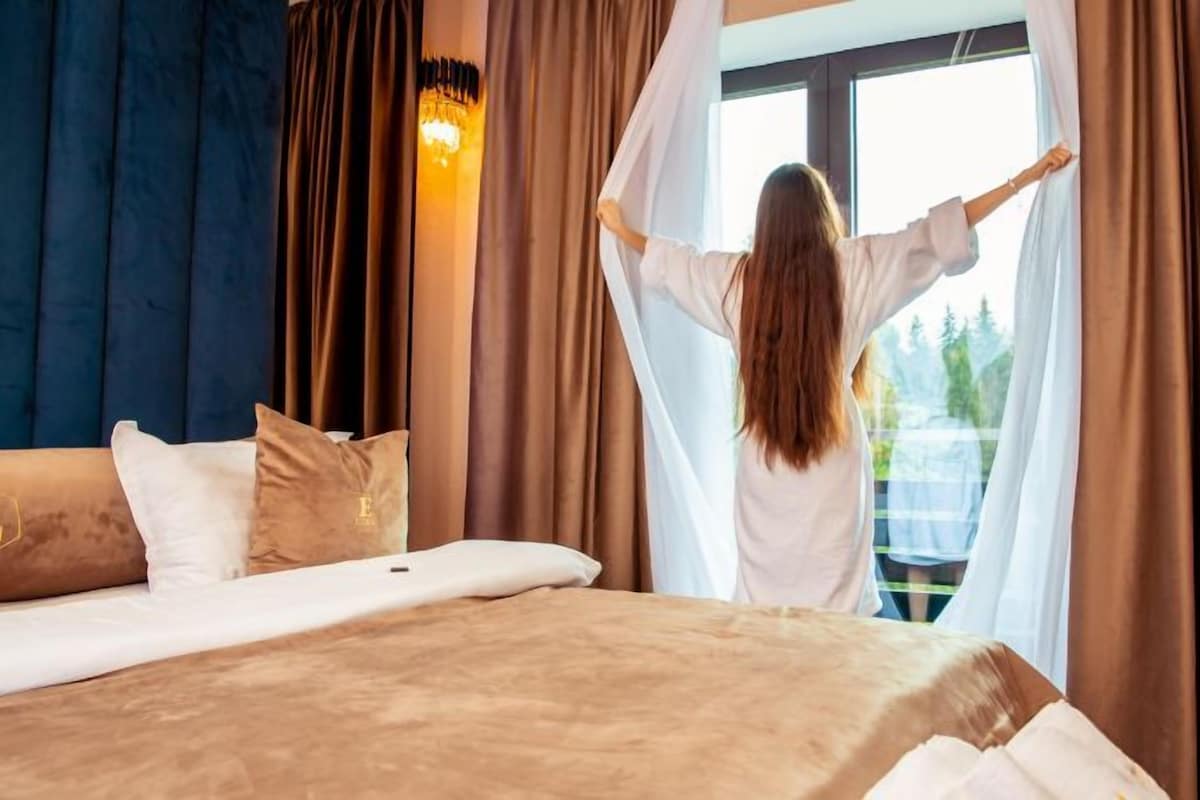A hotel room with a bed, a large window, and curtains.