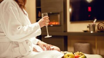En person i en vit dräkt som sitter vid en öppen spis med ett glas vin och en fruktskål.