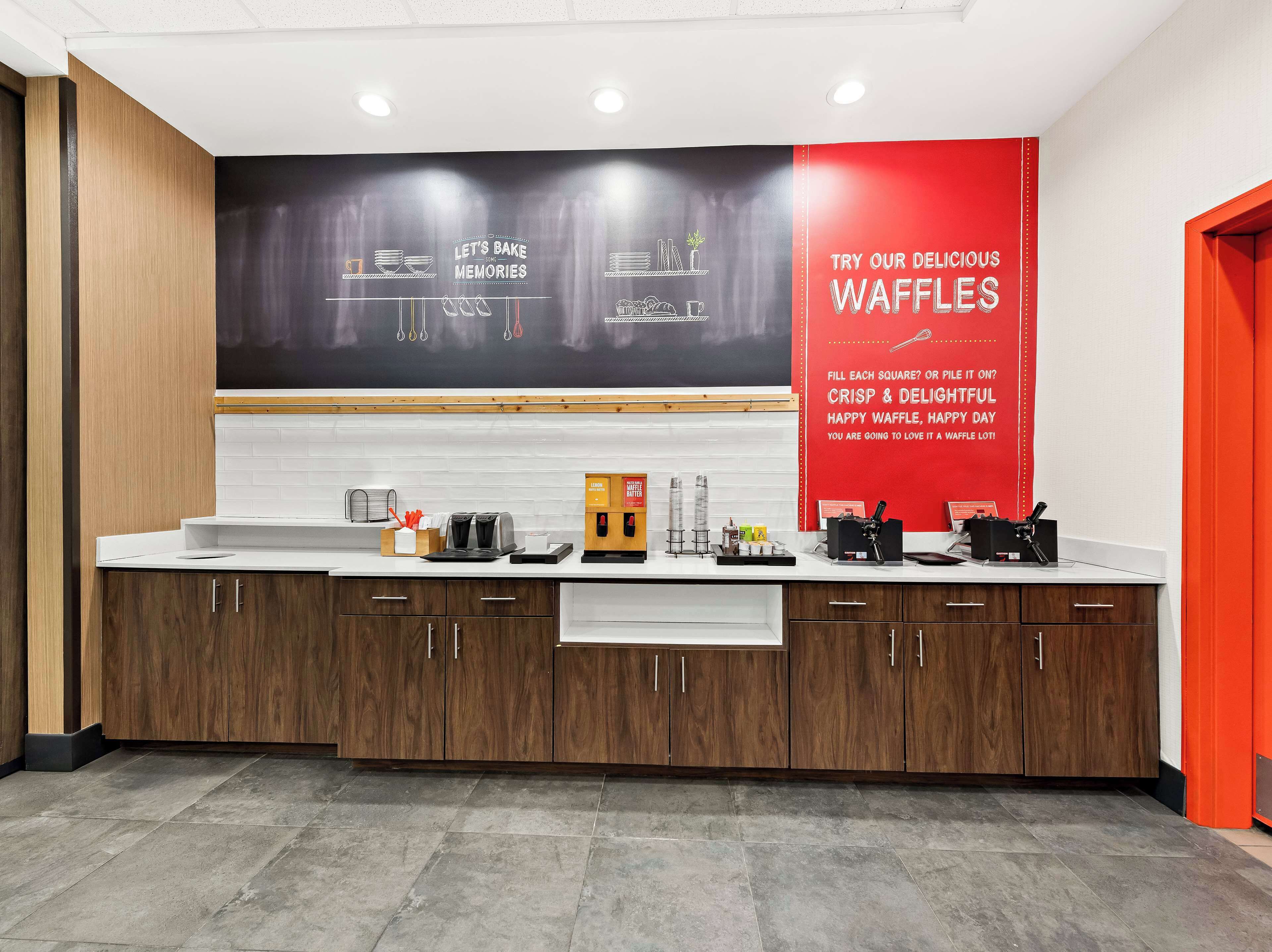 Une cuisine moderne dotée d’un grand tableau noir servant de panneau publicitaire pour les gaufres, d’une machine à café et de divers appareils de cuisine.