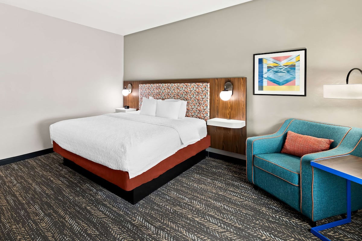 A hotel room with a bed, a nightstand, a wall-mounted light, a sofa, and a framed picture.