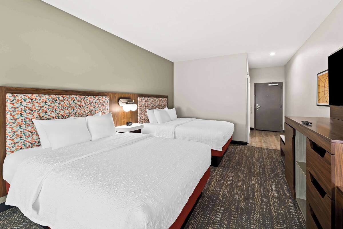 A hotel room with two beds, a desk, and a TV.