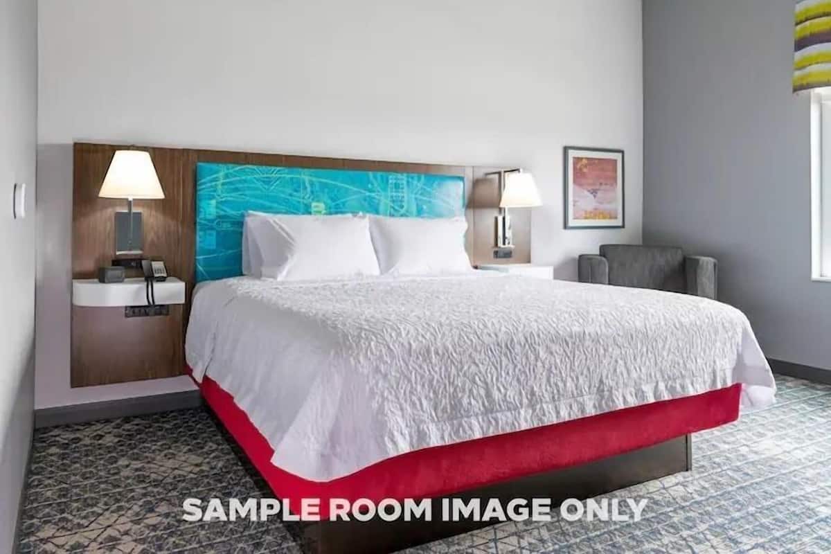 A hotel room with a bed, two bedside tables, a headboard, a wall-mounted TV, and a window with curtains.