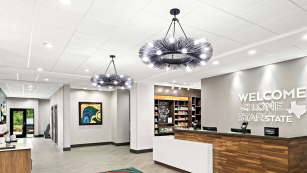 A modern hotel lobby with a reception desk, a colorful abstract painting, and a sign welcoming guests to the Lone Star State. - Hampton Inn Longview (Longview)