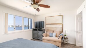 Quarto com cama, cômoda, televisão, cadeira e vista para a água.
