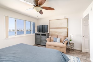 A bedroom with a bed, a dresser, a television, a chair, and a view of the water.