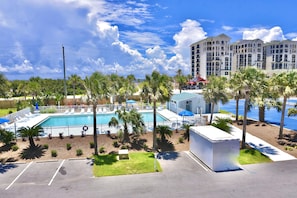 A hotel with a swimming pool, palm trees, and a parking lot.