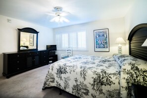 A bedroom with a bed, dresser, chair, and artwork on the wall. - A 22 Sundown Condominiums (Pensacola)