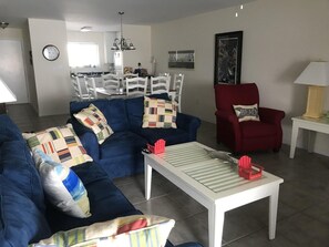 A living room with a blue sofa, a red armchair, a white coffee table, and a dining area in the background.