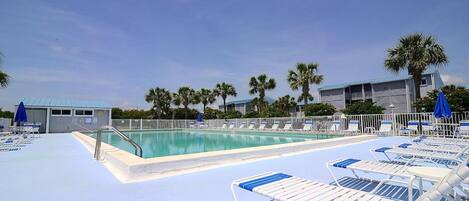 A pool area with lounge chairs and umbrellas, surrounded by palm trees and buildings.