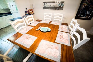 A dining table with six white chairs, each with a placemat featuring sea creatures. - A 22 Sundown Condominiums (Pensacola)