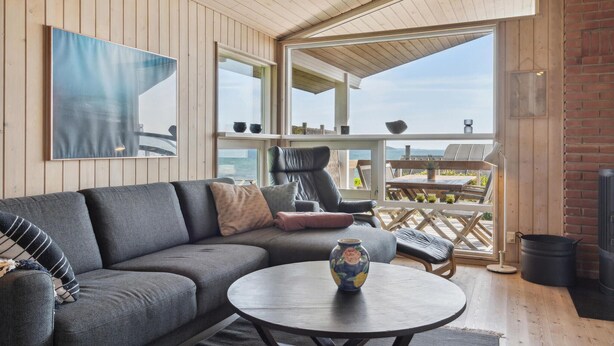 Una sala de estar acogedora con un sofá gris, una mesa de centro redonda y vista al mar a través de amplios ventanales.