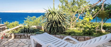 A stone patio with white lounge chairs overlooking a coastal view.