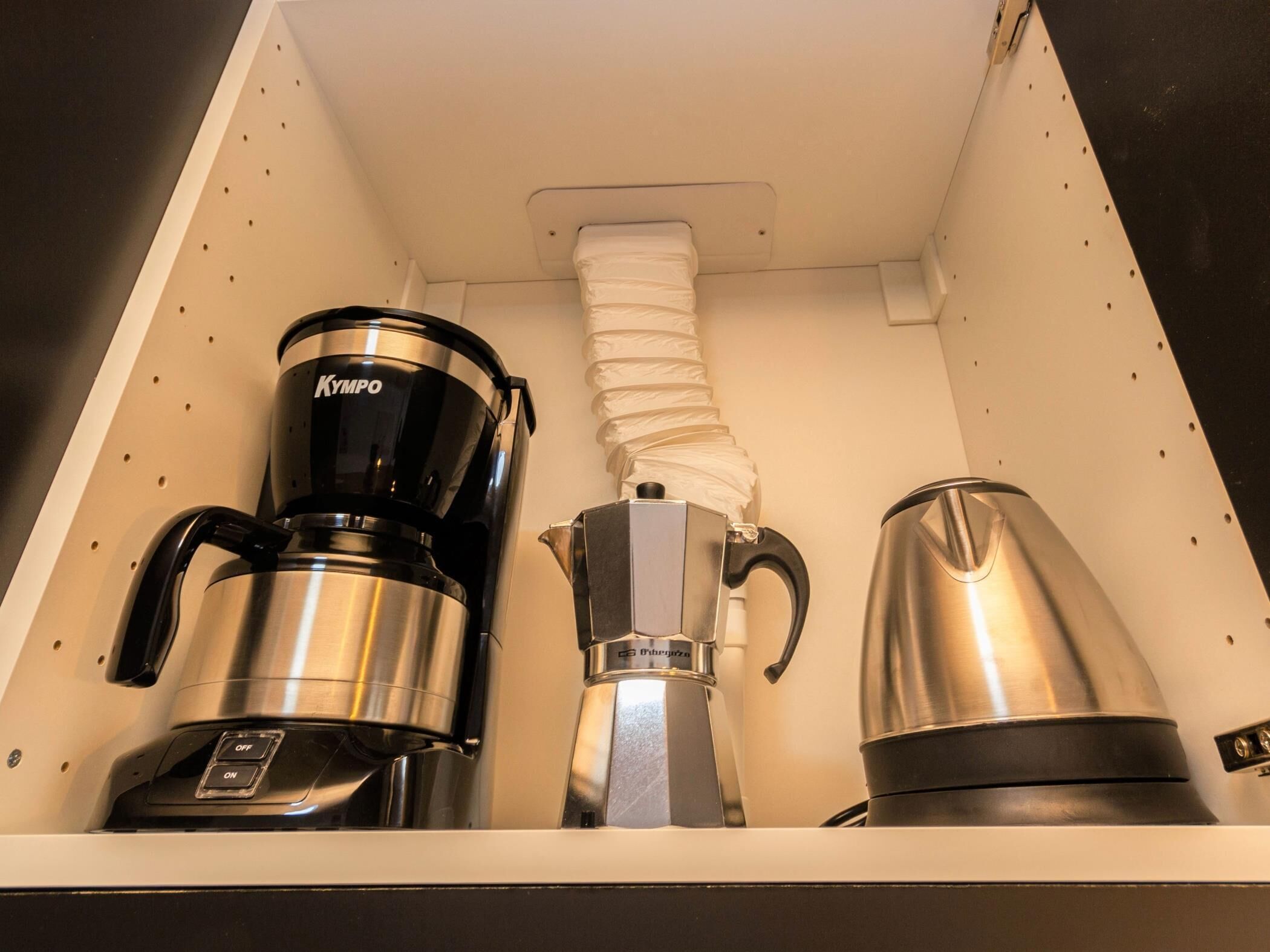 A coffee machine and a kettle in a kitchen cabinet.