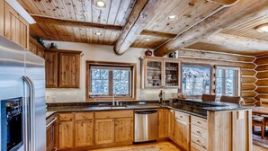 Ein Holzblockhaus-Innenraum mit einer Küche, die Holzschränke, einen Edelstahlkühlschrank, einen Geschirrspüler und eine Arbeitsplatte aus Granit umfasst.