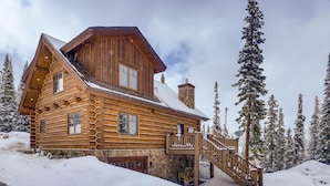 Eine Blockhütte mit einem Steinkamin, einer Holzterrasse und einer Treppe zum Eingang.