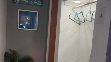 A hallway with a sign reading "La vida es bella," a framed picture, a potted plant, and a relaxation area with a towel and a basket.