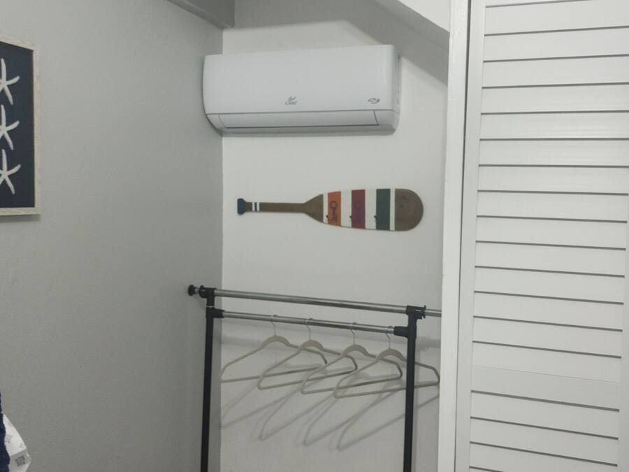 A small room with a bed, a wall-mounted air conditioner, a drying rack with clothes, and a basket.