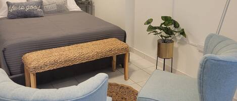 A modern bedroom with a bed, two armchairs, a bench, a wall-mounted TV, and a decorative fish wall art piece.