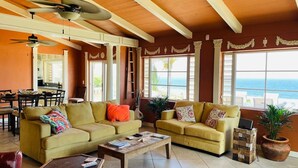 A spacious living room with two sofas, a coffee table, and a dining area with a view of the ocean. - Caribbean Island Retreat, 200 degree water views, trade winds and soothing waves (Christiansted)