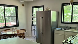 A modern kitchen with a large island, a refrigerator, and a dining area with a table and chairs. - Happy mtn. home, enjoy 7 acres & 2 ponds, 1/2 mile to DuPont State Forest gate! (Cedar Mountain)