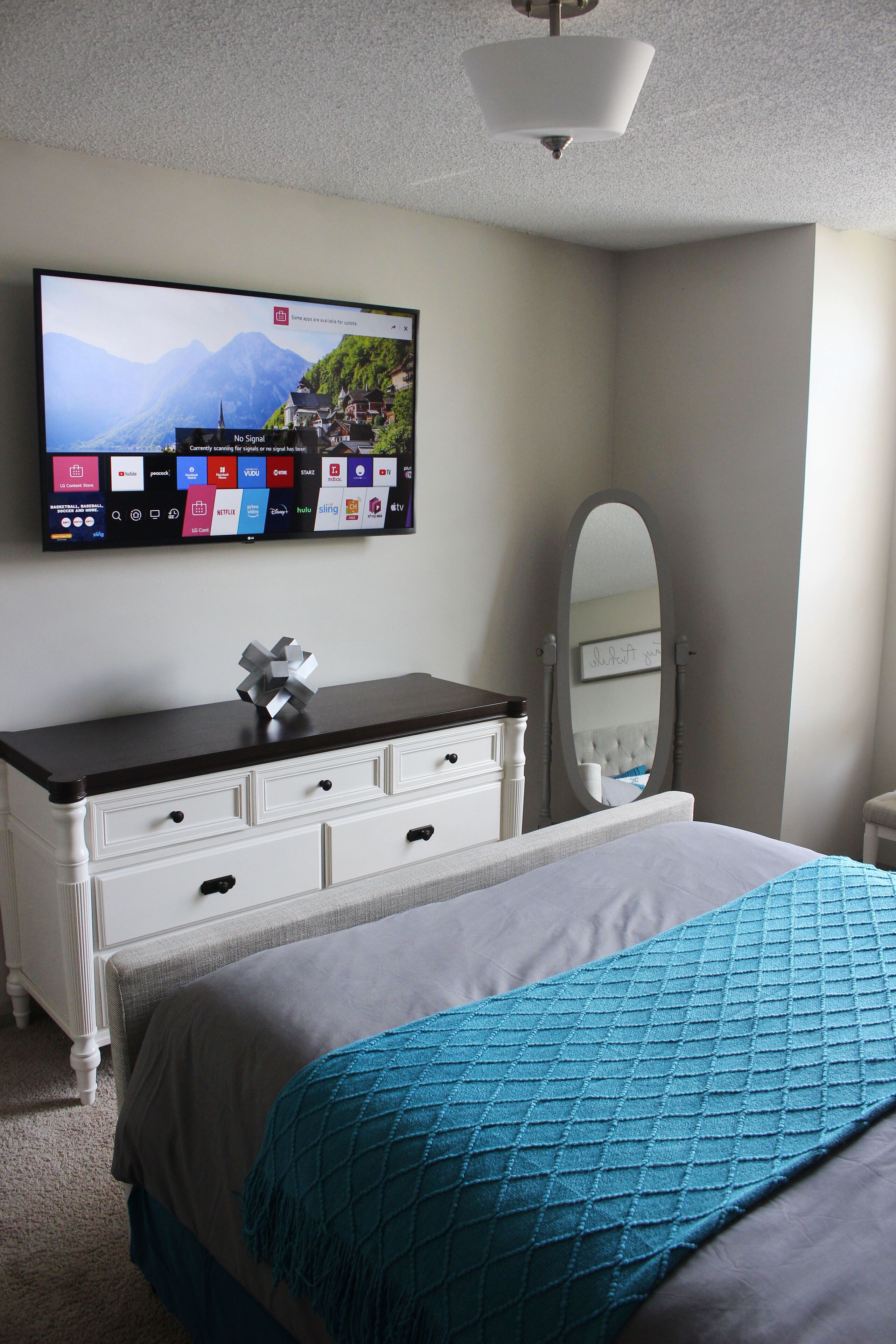 A bedroom with a bed, a dresser, a mirror, and a flat-screen TV mounted on the wall.