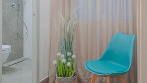 A bathroom with a shower, a toilet, a potted plant, and a teal chair.