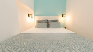 A bedroom with a bed, patterned pillows, and wall-mounted lights.