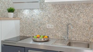 A modern kitchen with a granite backsplash, stainless steel appliances, and a bowl of fruit on the counter.