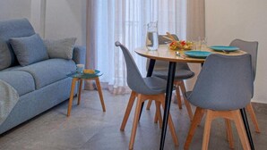A dining area with a round table, four chairs, a hanging light fixture, and a sofa.