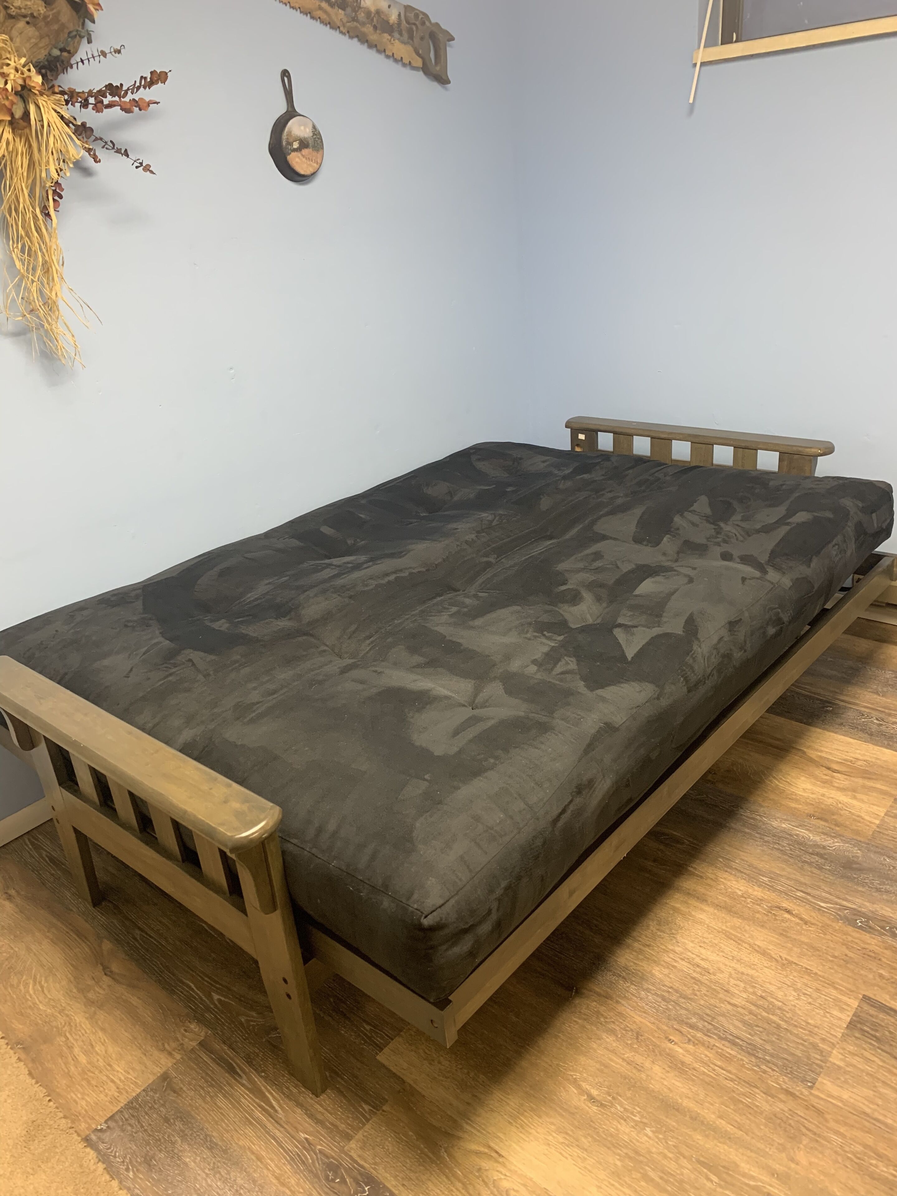 Ein Einzelbett mit einem Matratze im Tarnmuster, ein Holz-Kopfende und ein Fußteil, vor einer hellblauen Wand.