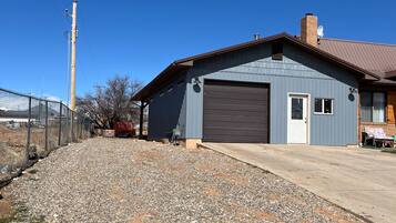 Un edificio a un piano con garage, vialetto sterrato e area recintata.