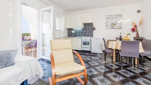 Eine kompakte Küche mit weißen Schränken, einem Herd und einer Spüle. Es gibt einen Essbereich mit Tisch und Stühlen, und ein Sofa im Vordergrund.