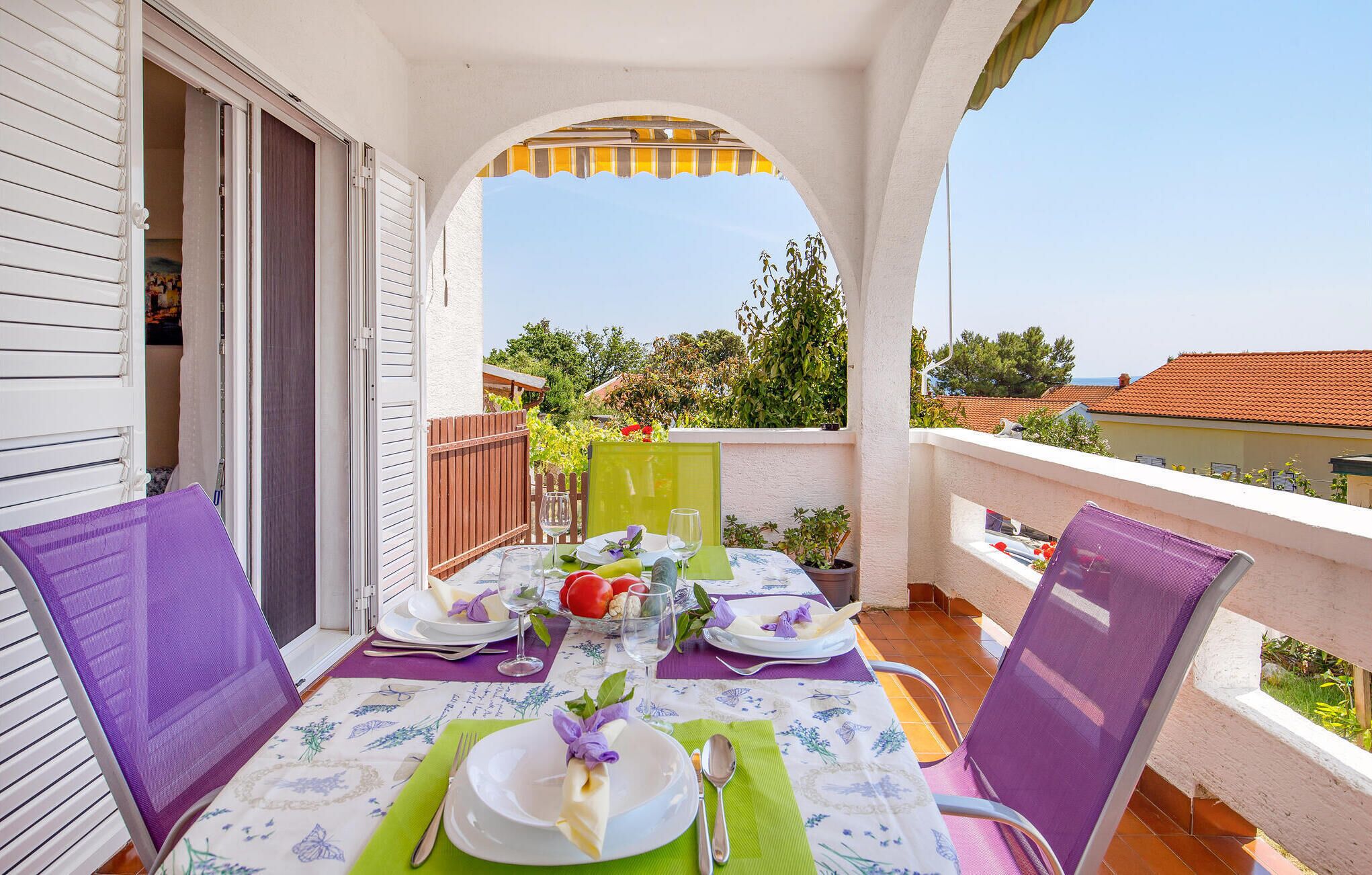 Varanda com mesa posta para dois, com vista para o mar e vegetação ao redor.
