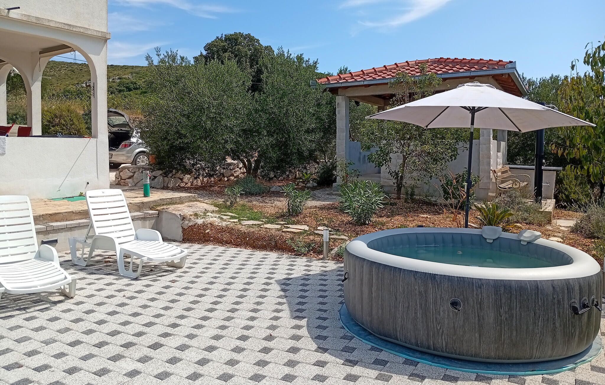 An outdoor hot tub area with a tiled patio, lounge chairs, and a pergola with an umbrella.