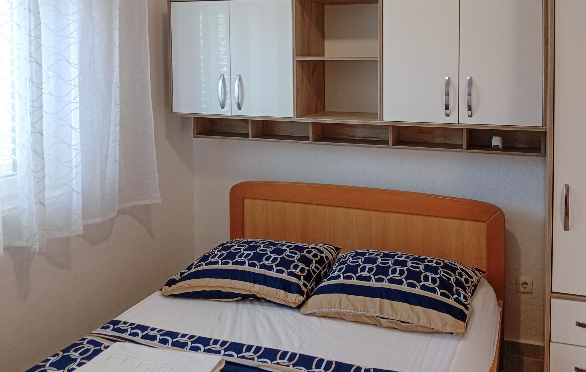 Un dormitorio con cabecera de madera, cama con ropa de cama estampada, dos almohadas y un armario con puertas de espejo.