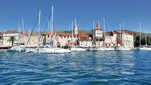 Un puerto deportivo con varios veleros amarrados, un edificio histórico con una torre de campanas y un cielo azul despejado.