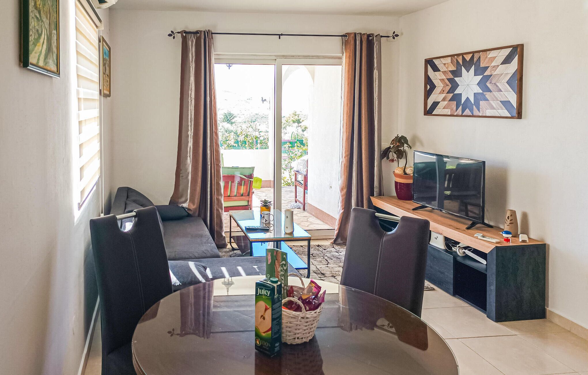 Un salon avec une table en verre, deux chaises noires, un canapé, un téléviseur et un tableau accroché au mur.